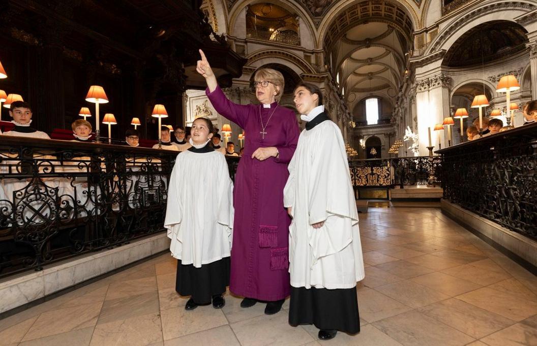 Dame Sarah Mullally and two female choristers standing in catherdral.