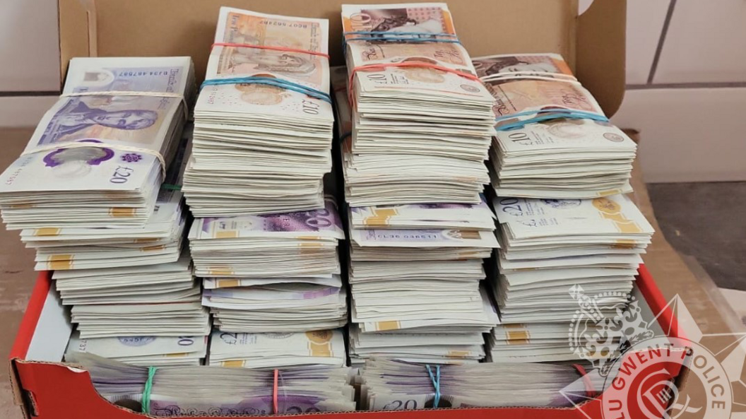 A picture of piles of banknotes bundled and secured with elastic bands in a red Nike shoe box. The lid can't be closed because the piles are so tall.