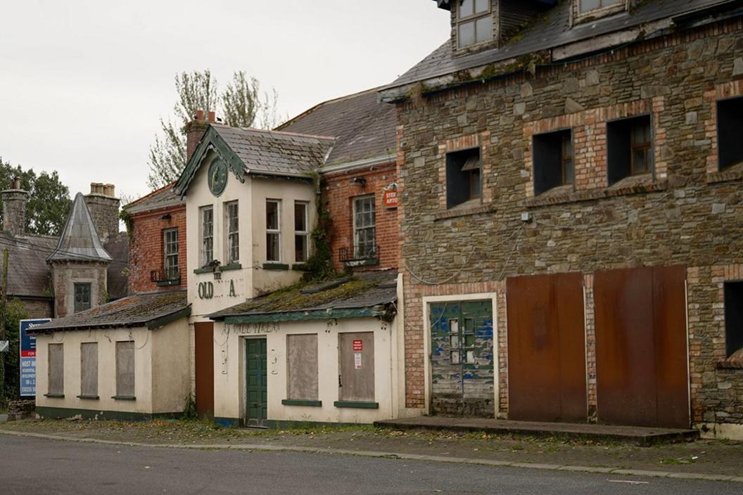 A run-down, once handsome building with a white facade, boarded up windows and broken signage - the remaining letters read "..OLD...A.." 