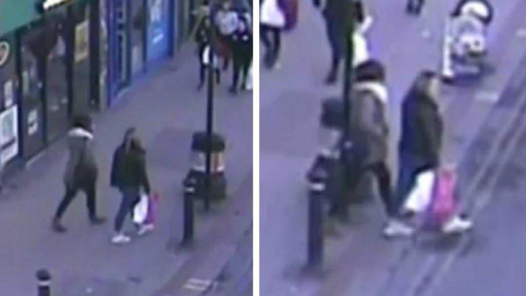 A still of CCTV footage shows two women walking down a road with shops.