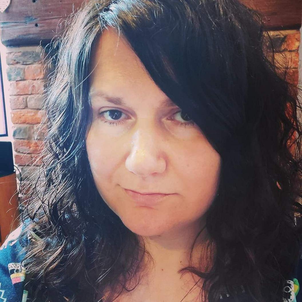 A head shot of a woman with long black hair, standing in front of a brick wall.