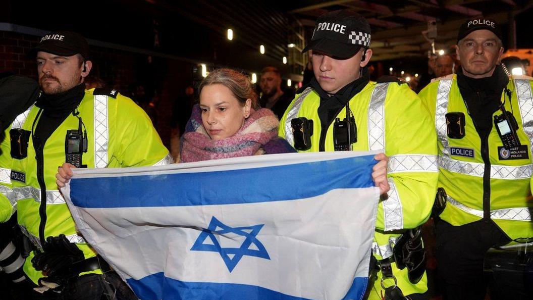 A women named Emily carrying an Israel flag is moved away by police officers from pro Palestine campaigners, who are protesting on Trinty Road outside Villa Park.