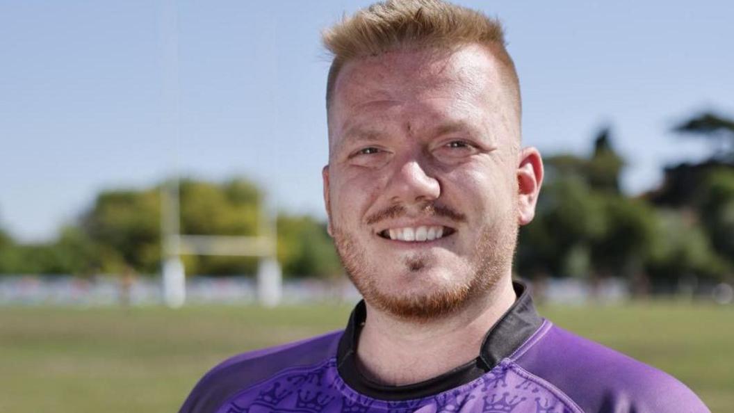 Sam Biscoe in a purple top smiling at the camera 