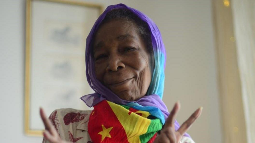 Marline Anderson, wrapped in the Grenada flag makes peace signs with her hands 