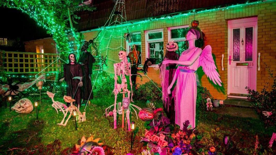 The garden of a yellow brick bungalow is covered with skeletons, a pumpkin-headed figure and a mannequin dressed as an angel.