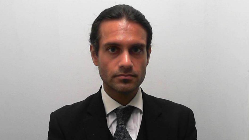 Custody picture of a man with tied up dark hair, wearing a three-piece suit