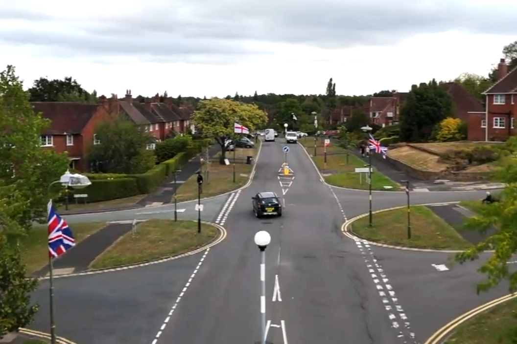 Union Jack and St George flags hang from every lamppost on a street in Birmingham, seen from an aerial drone shot.
