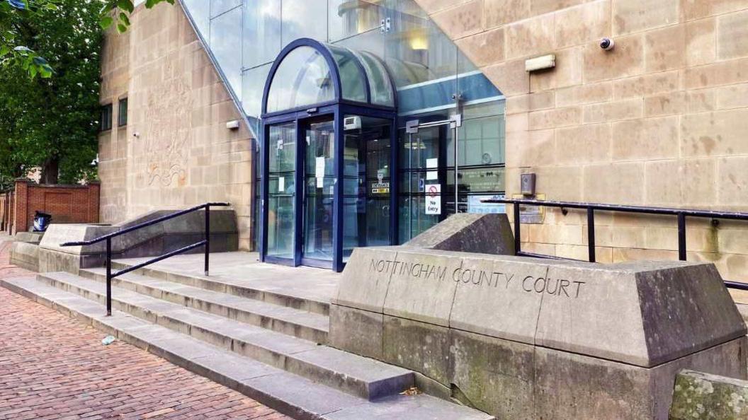 The exterior of Nottingham Crown Court which is a light brick building with a glass frontage and blue-framed glass doors.