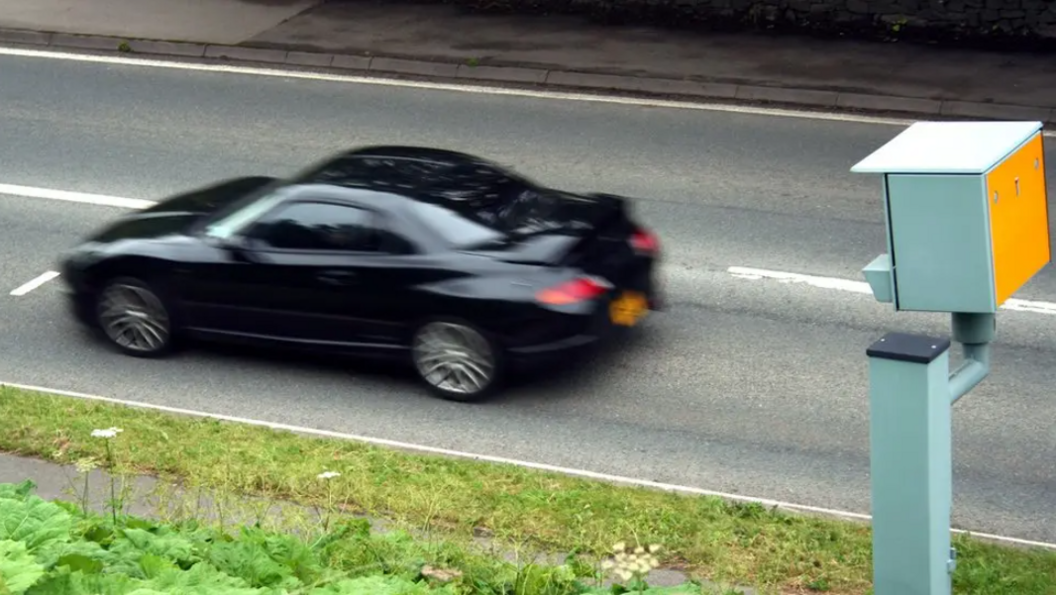 A slightly blurred image of a black car speeding past a speed camera