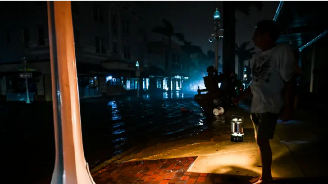 Man stood holding a lantern in a pitch black neighbourhood.