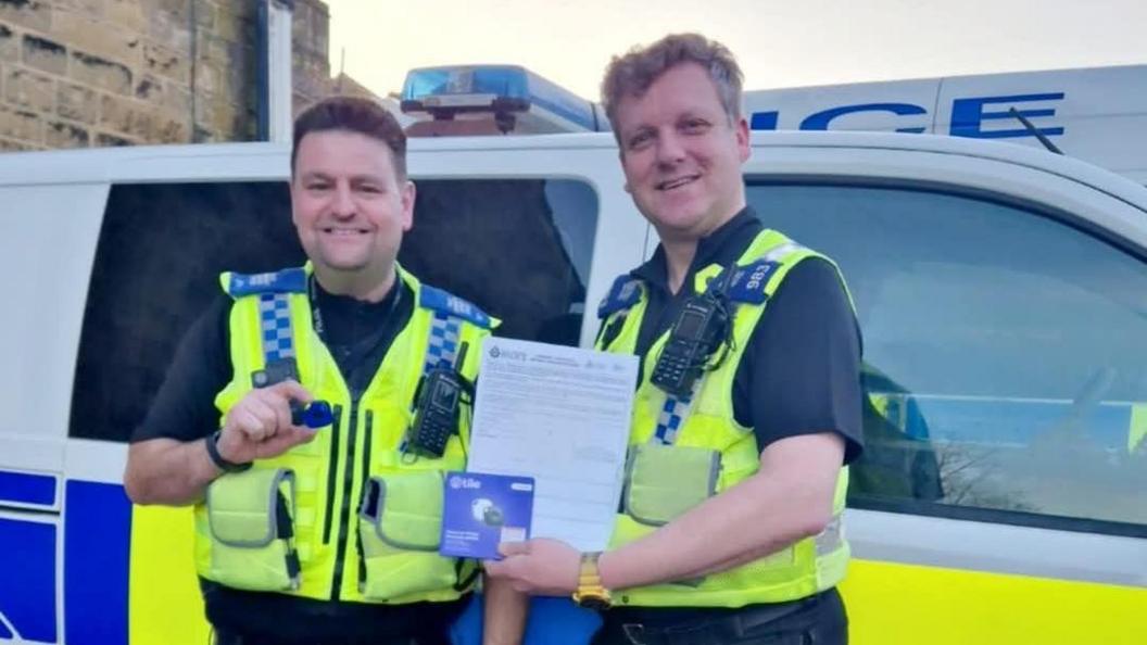 PSCO's Ben Verdeyen and Matt Veall from Shipley's neighbourhood policing team. Both are wearing reflective police vests and have radios. Behind them is two police vans. 