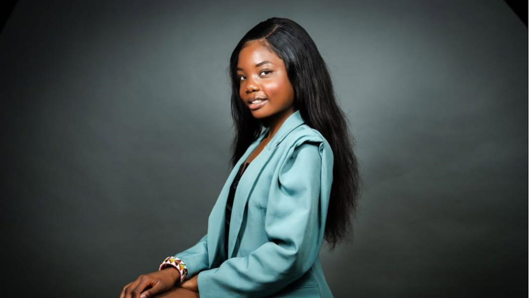 Shows a woman with long black hair, jade-coloured jacket and dark top with a colourful bracelet on her right wrist