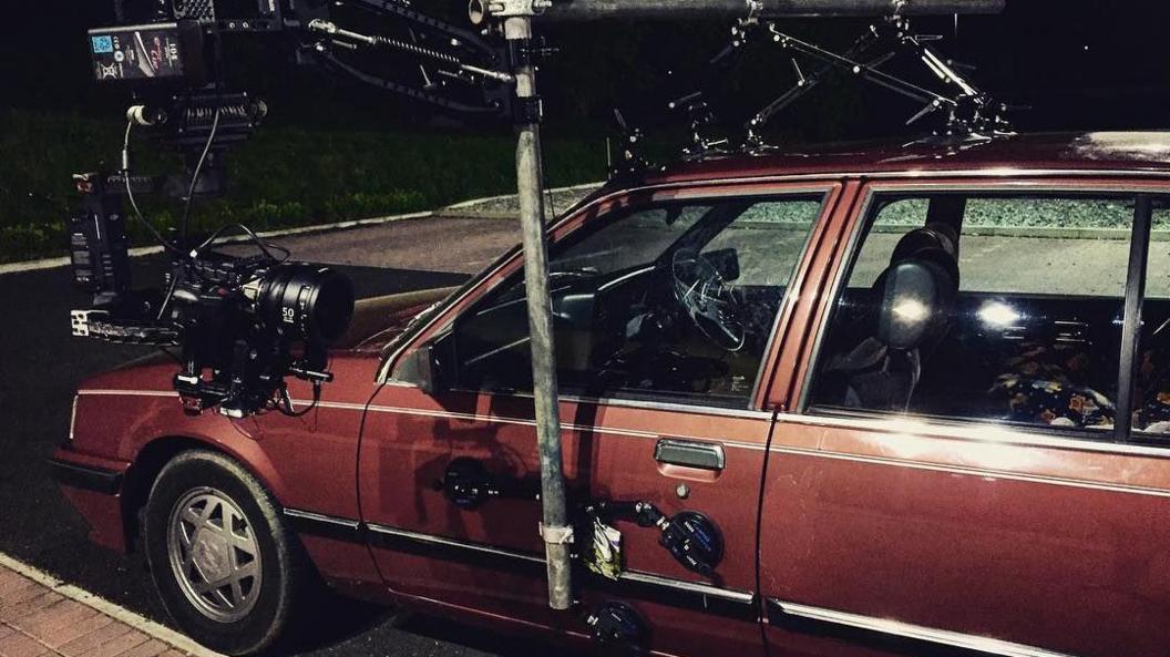 An old red car with a camera mounted to the side for filming