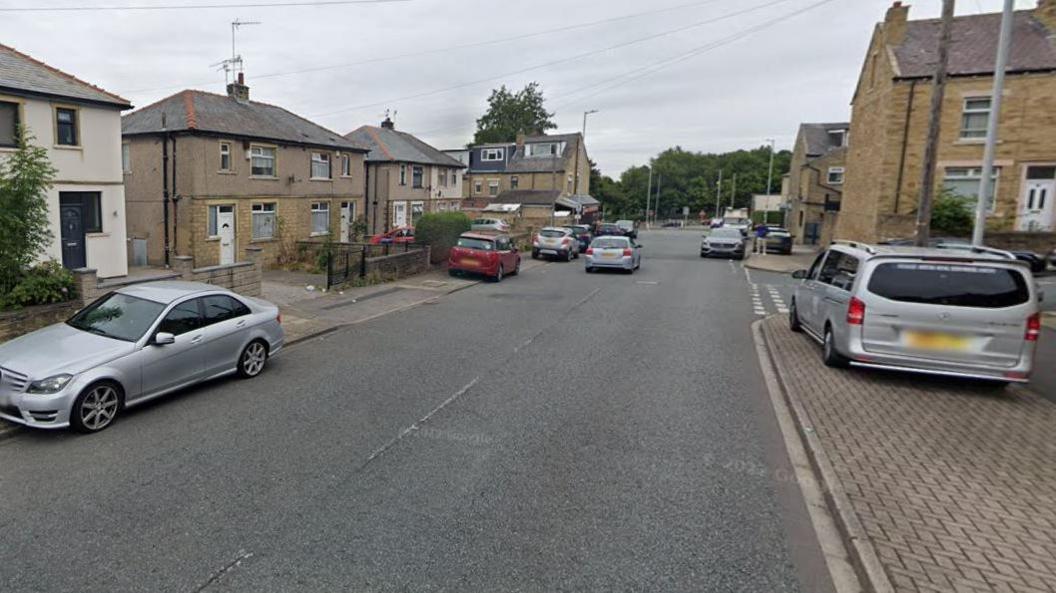 An image of a road with semi-detached houses either side. A silver Mercedes is parked half on the curb and half on the road to the left of the picture and a silver van is parked on the path on the right.