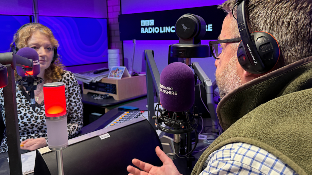 A behind the shoulder view of Richard Davies talking to Frances Finn, Frances has ginger curly hair and is wearing a leopard print shirt.