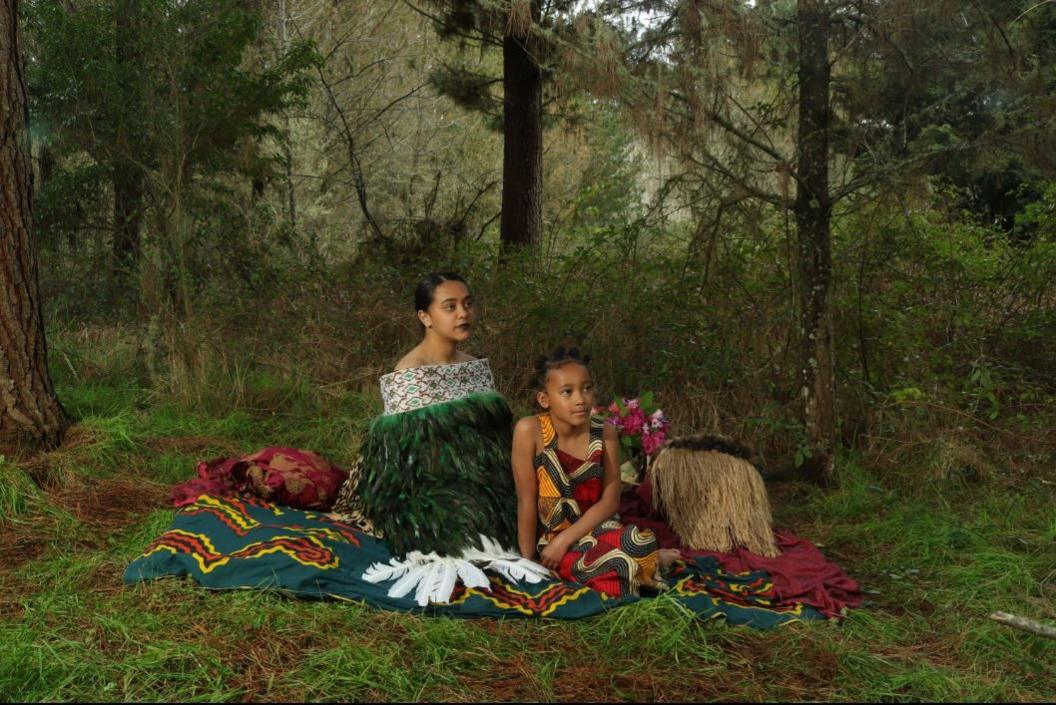 Two girls dressed in traditional Igbo and Māori garments and accessories.