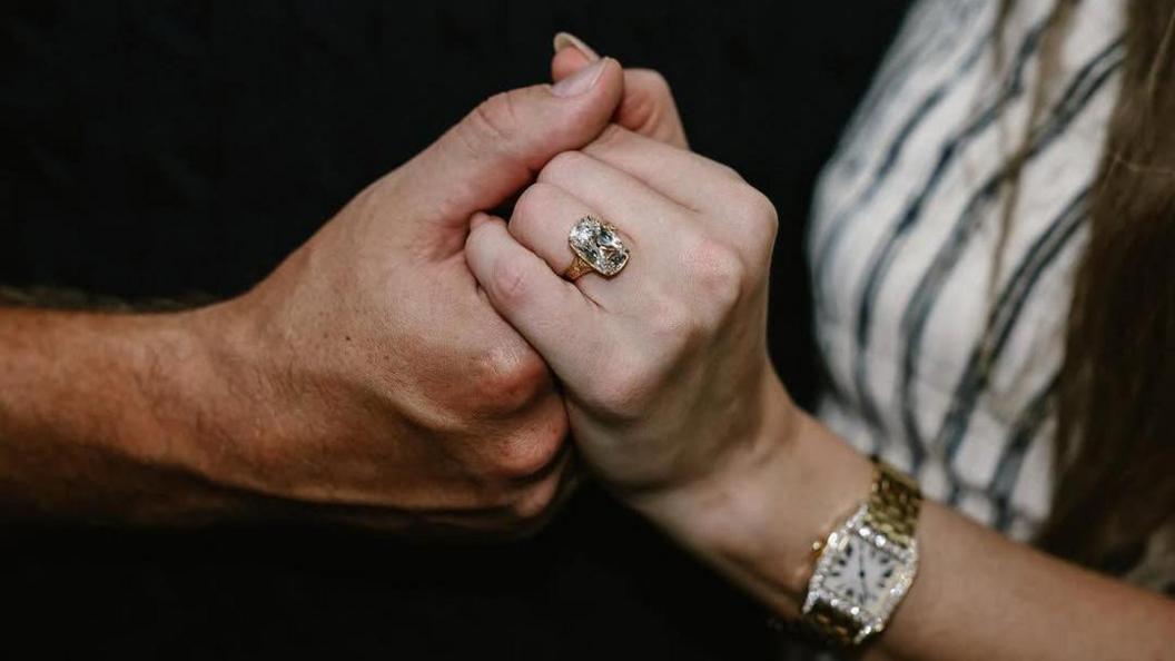 Kelce's hand holding Swift's hand, and her ring, which is big and sparkly, is visible on her ring finger. She also wears a gold watch with diamonds.