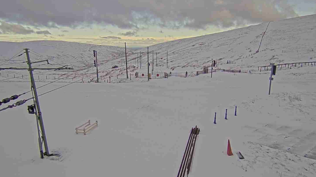 A view of Laxey Valley covered in snow, with poles for the tram lines visible and the sun is setting in the background.