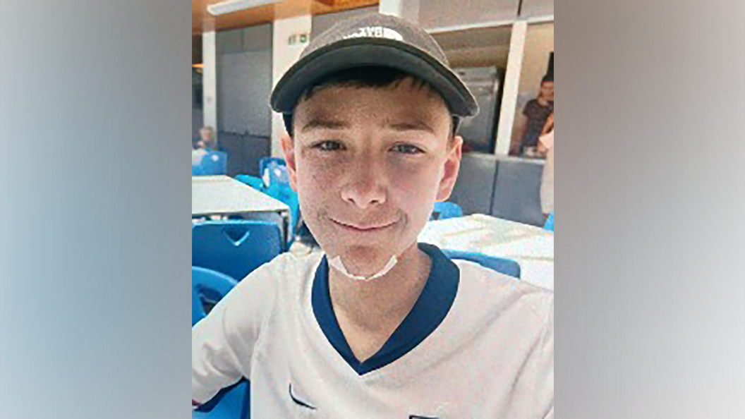 Mylo smiling into the camera. He is wearing a grey cap and England football shirt. He has a plaster on his chin.