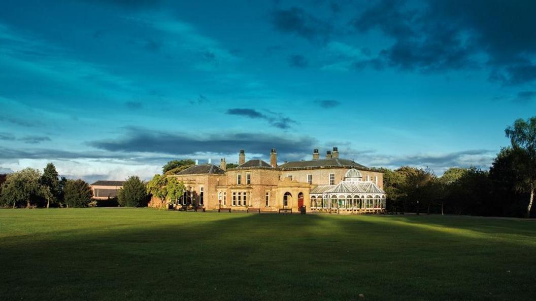 Preston Park Museum & Gardens main Victorian building with its domes glass conservatory pictures on a sunny evening with long shadows from the trees over the grass lawn and a moody blue sky overhead.