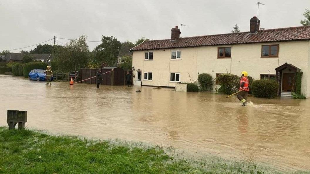 A street is flooded with emergency services walking through the new river of brown water