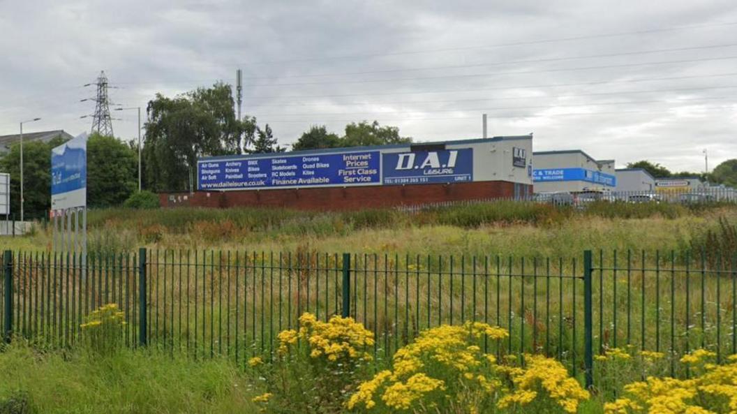 A warehouse with a large blue sign that says DAI Leisure in white writing. The warehouse is in a row of similar buildings.