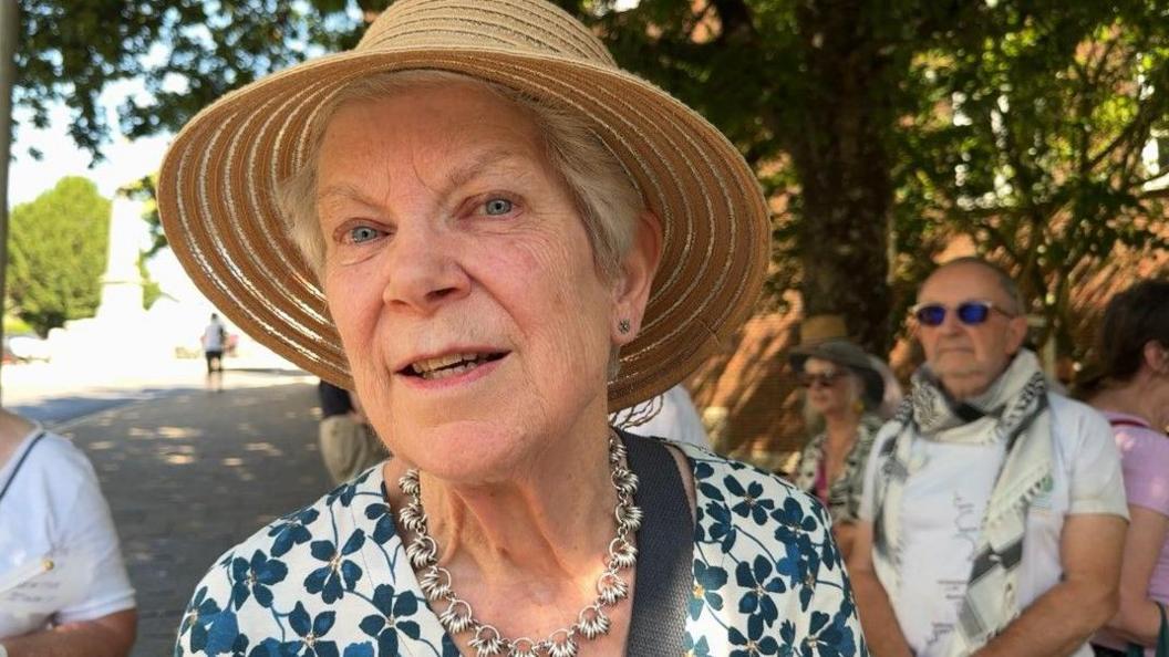 Jenny Streat wearing a summer hat and a flowery dress looking at the camera