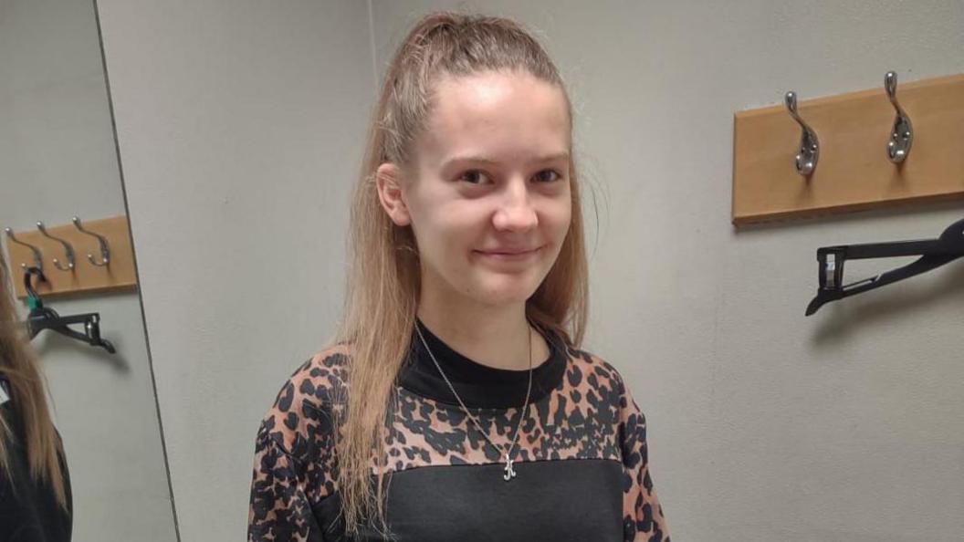 A girl with long blonde hair and a leopard-print top smiling at the camera