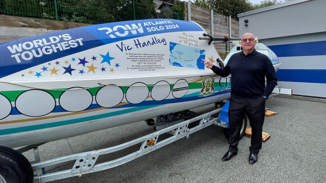 A bald man with glasses stood pointing at a white boat