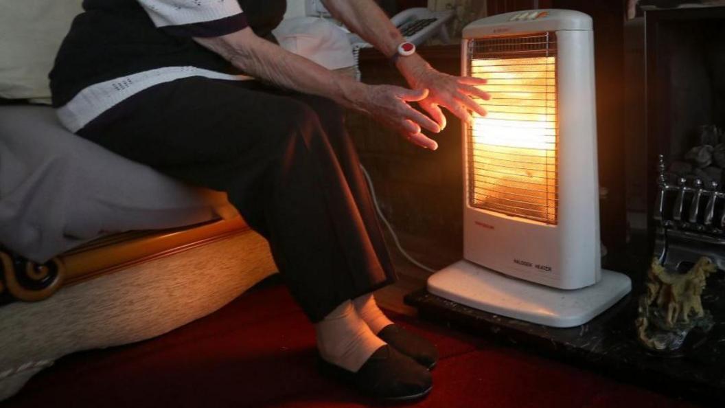 A file image of a pensioner warming her hands in front an electric heater