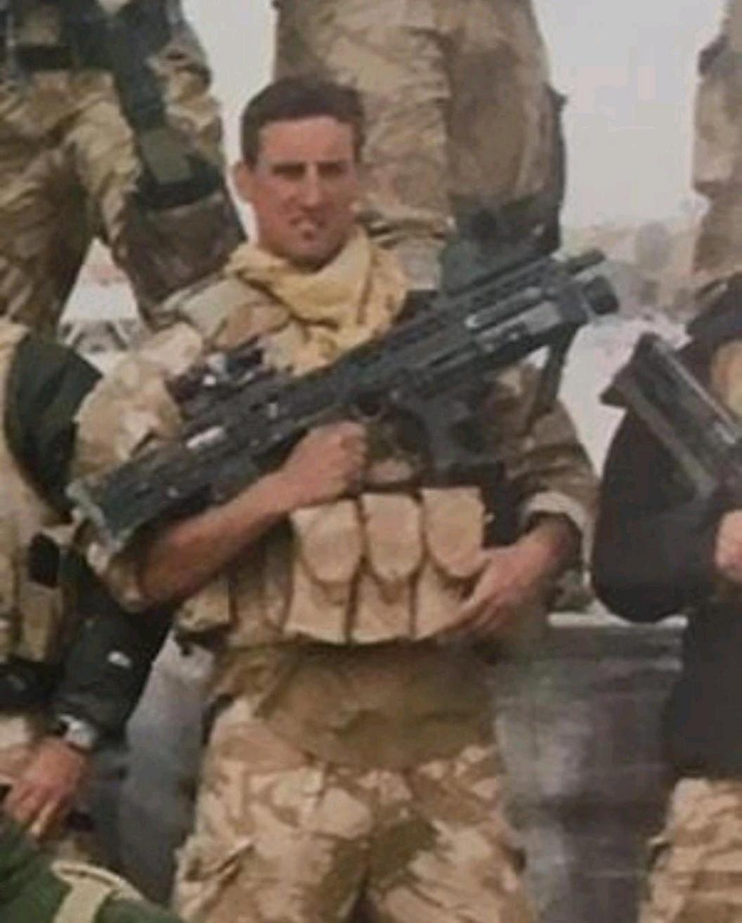 Ben in desert camouflage uniform in Afghanistan. He is holding a machine gun. 