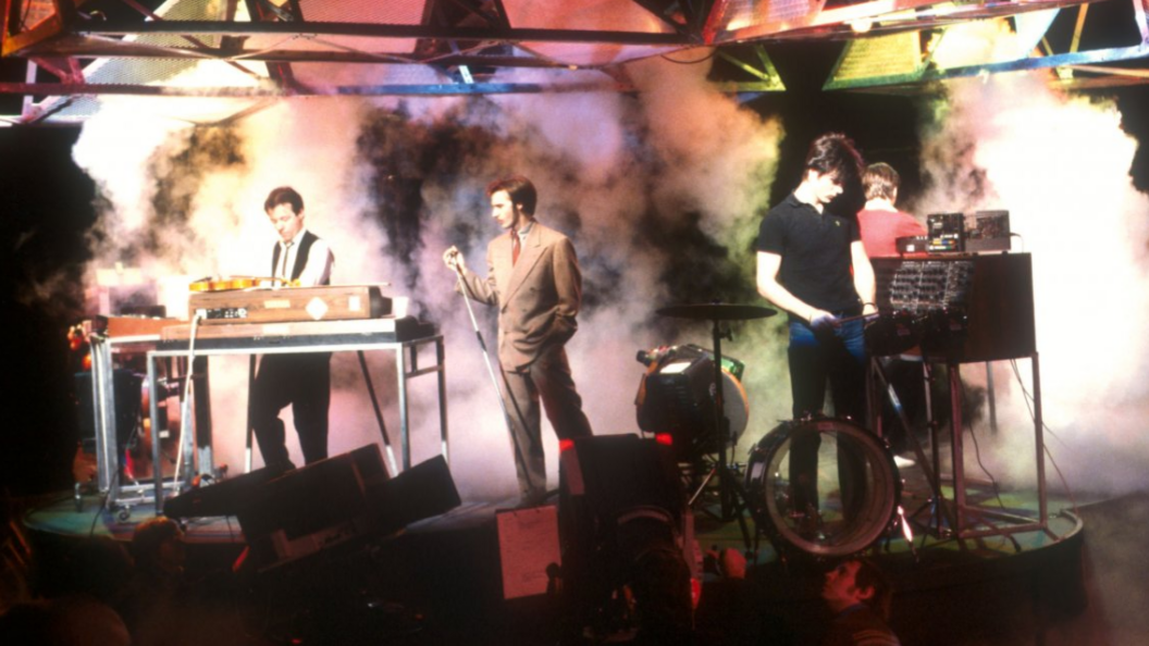 An old photograph from the 1980s of the band on a stage with smoke machines creating coloured smoke