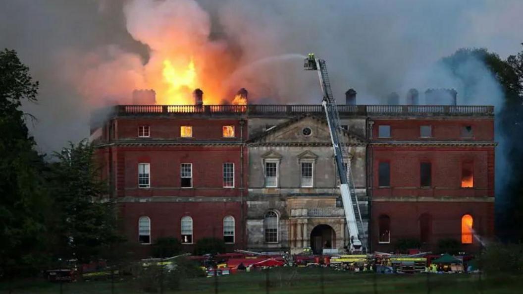 Exterior shot of fire ravaging Clandon Park in 2015 with fireman and fire engines and ladders tackling the blaze 