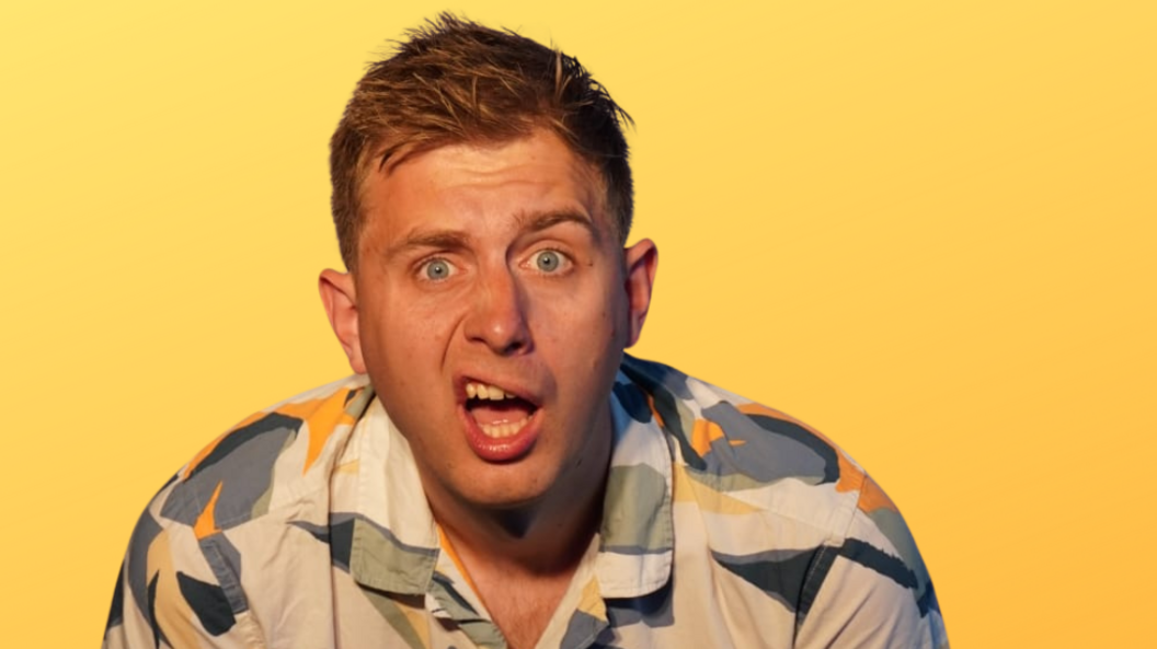 Martin Westgate wearing a colourful shirt and sneering as part of a promotional photo. He has short brown hair, blue eyes and is standing in front of a yellow background