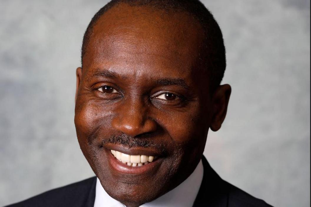 James Williams smiles at the camera in a black suit and white shirt