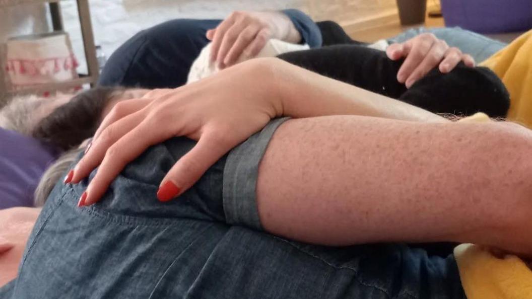A group of people are tightly locked in a cuddle. Their faces are not visible but their arms and hands are tightly wrapped around each other.