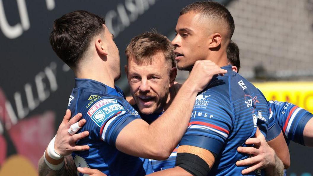 Tom Johnstone is surrounded by team-mates, all in Wakefield Trinity blue, as they celebrate one of his three tries against Bradford Bulls.