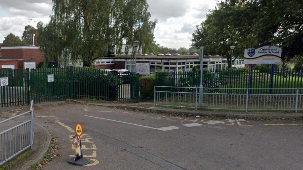 The entrance to Chetwynd Junior School, with railings around the footpath and a white sign with the school crest and contact information on it.