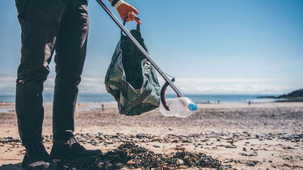 man picking litter from the beach