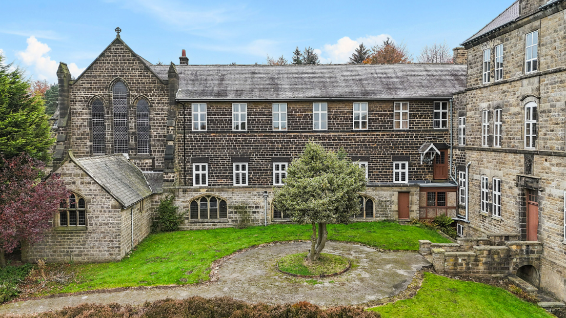 A brick-built building from the 1800s. It has white-crossed window frames and has a tree in an island-setting in the middle.