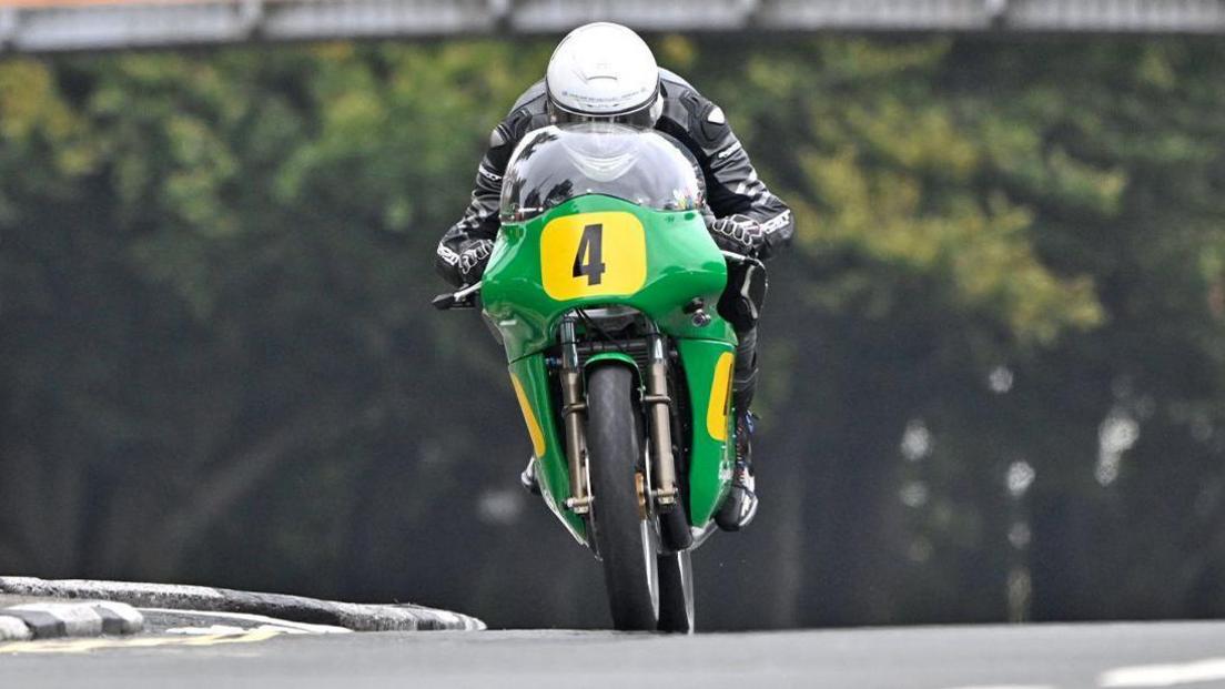 Shaun Anderson riding on a green bike with yellow plates featuring the number four in black lettering. He's wearing black leathers and a white helmet.