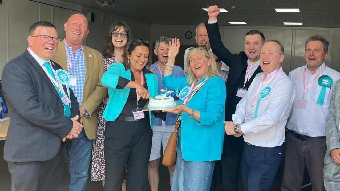 A group of Reform UK councillors and supporters celebrate election victory in Maidstone in May 2024, by cutting a cake.