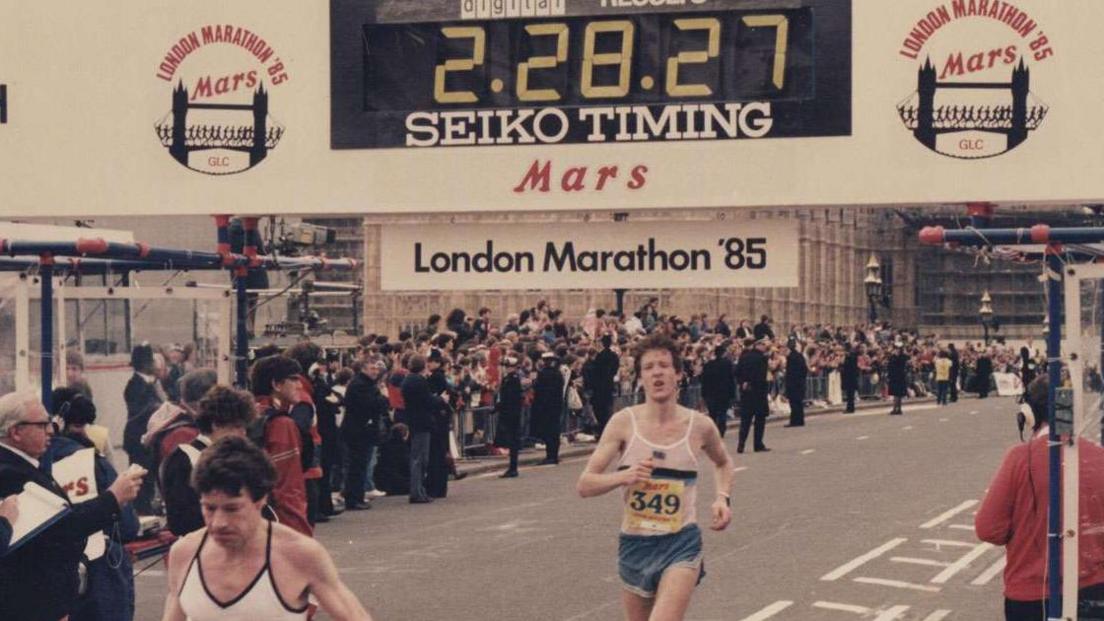 Chris at the finish line with a clock that says 2 hours and 28 min.