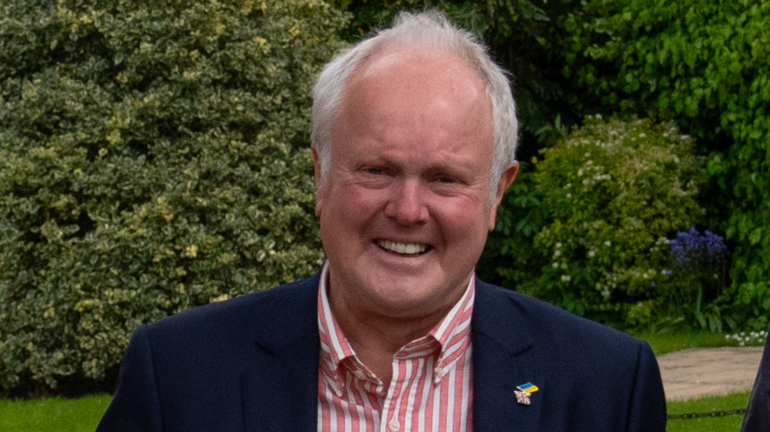 Clive Jones, the Wokingham Lib Dem candidate at the time of April 2024, wearing a Ukraine/UK badge on his jacket's lapel and white and pink shirt. He has short, white hair and is smiling at the camera.