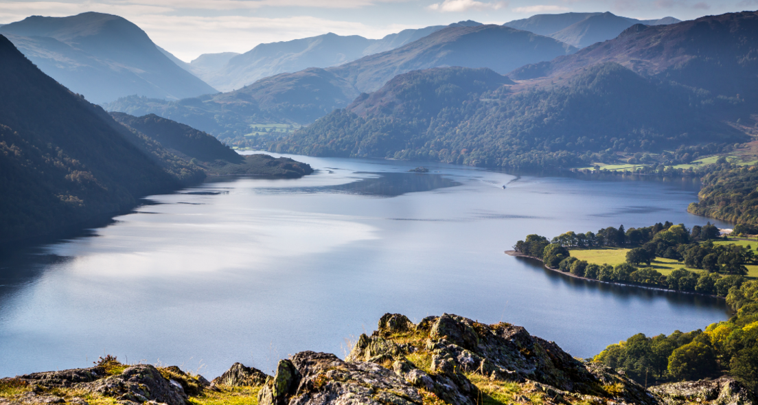 A general view of Ullswater in the Lake District. It is looking down on the lake with a vista of interlinking mountain peaks stretching into the distance.