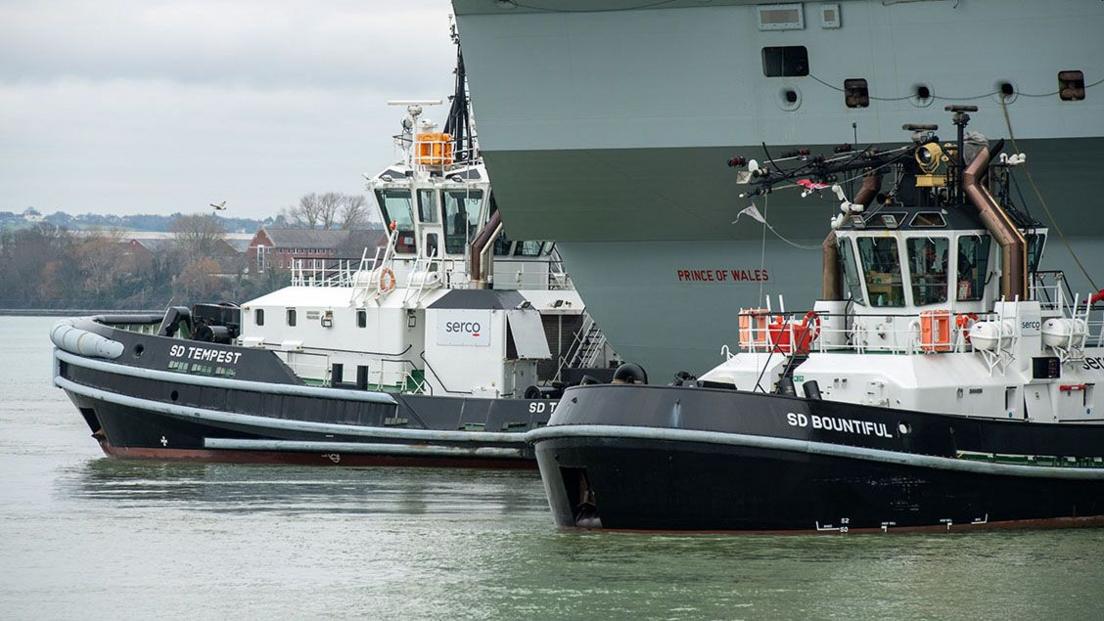 Two tugs beside an aircraft carrier Prince of Wales