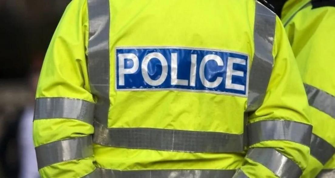 The back of a police officer wearing a fluorescent yellow coat with the word POLICE in capital letters.