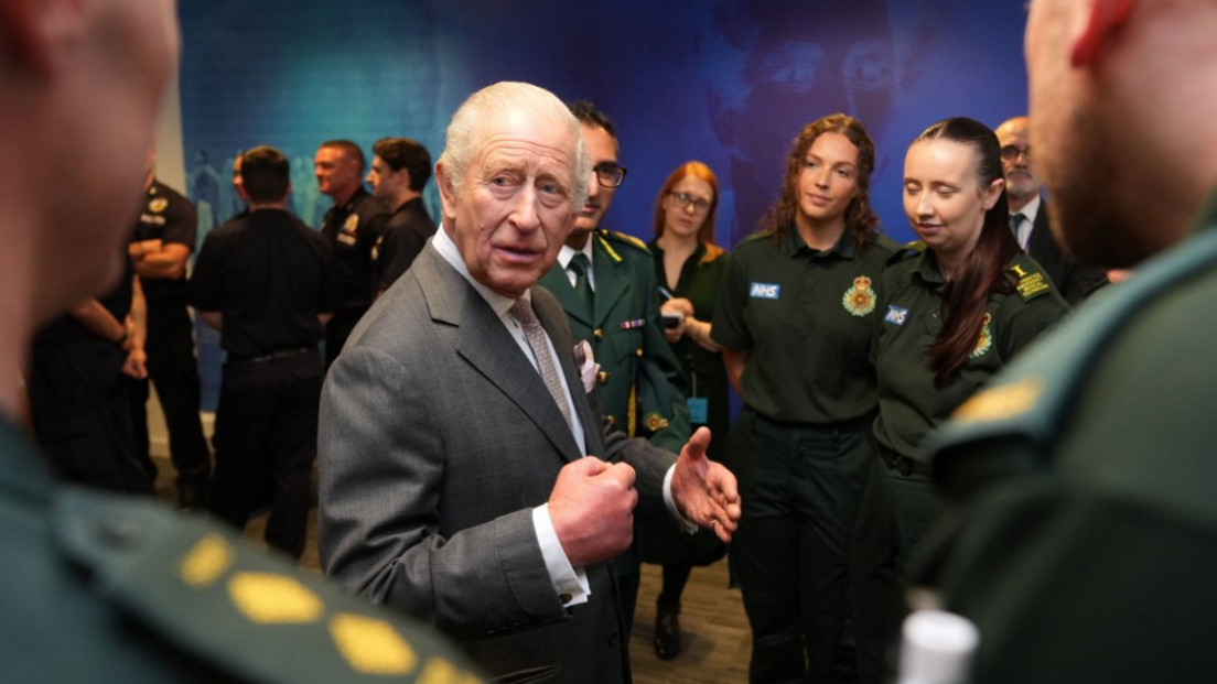 The King is surrounded by ambulance staff, wearing green uniforms