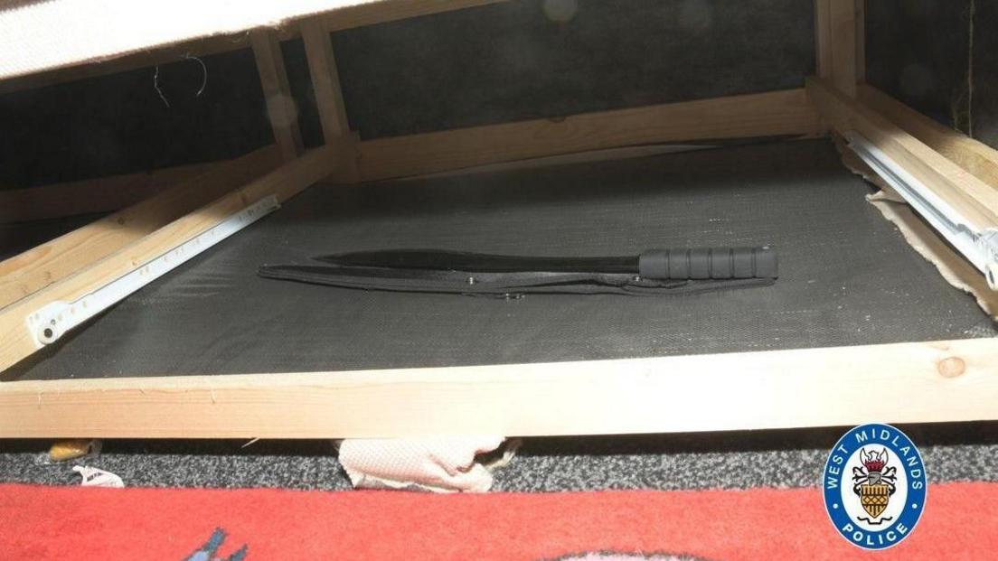 A machete lies under a bed