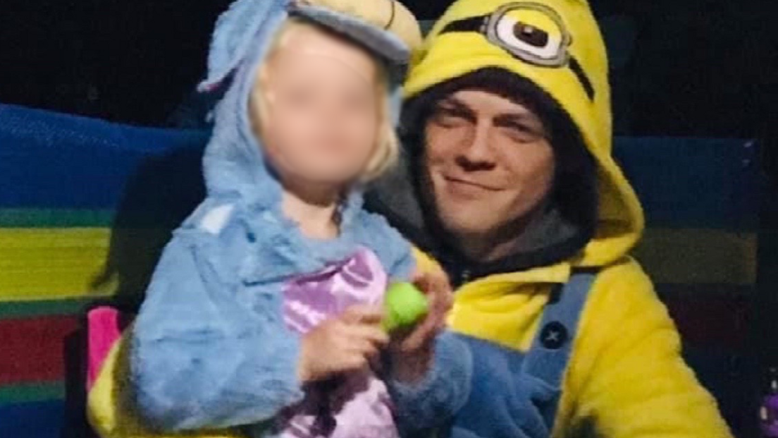 Andrew Main hugging one of his daughters. She is wearing a blue coat and he is wearing a yellow Minions outfit.